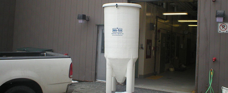 Dura-Tech fiberglass conical bottom tank positioned outside manufacturing facility with company logo visible