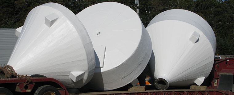 Three large white fiberglass conical bottom tanks being transported on a flatbed trailer