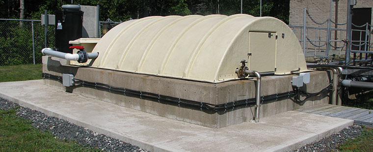 Dura-Tech fiberglass domed cover installed over wastewater treatment tank with concrete base and piping connections