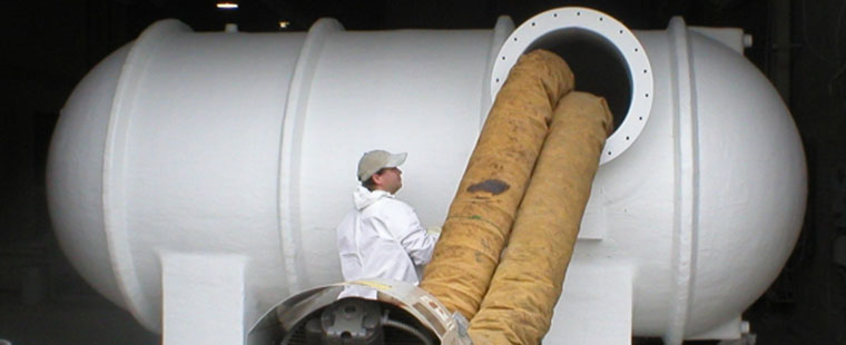 Dura-Tech worker installing large white fiberglass horizontal saddle tank with flexible ducting connections