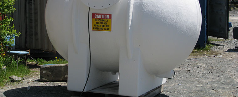 White fiberglass horizontal saddle tank with legs and caution label on concrete pad