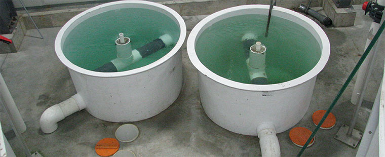 Two Dura-Tech fiberglass swirl separator tanks with green water and central standpipes at treatment facility