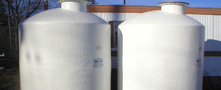 Two large white Dura-Tech vertical fiberglass storage tanks with top access ports at industrial facility